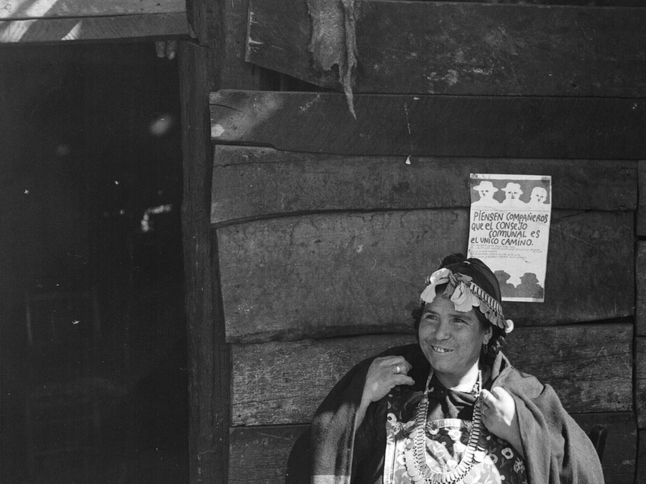 Temuco: Mujer mapuche (Amiga de Cardoso) sentada afuera de su ruca que tiene en la pared un afiche que dice: &amp;quot;Piensen compañeros que el Consejo Comunal es el único camino&amp;quot;. Sentada afuera de su ruca tocando un kultrú, con sus collares de plata; desta