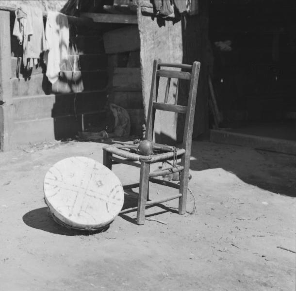 Temuco: Mujer mapuche (Amiga de Cardoso) sentada afuera de su ruca que tiene en la pared un afiche que dice: &quot;Piensen compañeros que el Consejo Comunal es el único camino&quot;. Sentada afuera de su ruca tocando un kultrú, con sus collares de plata; desta